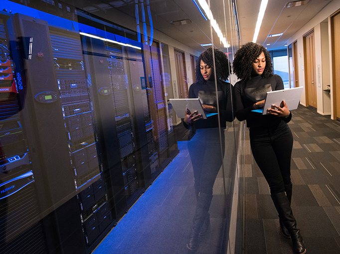 A woman standing behind a data centre holding a laptop